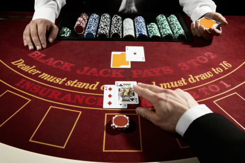 Black Jack hand showing King and number 6 on a red casino table. Asking dealer to get another card.