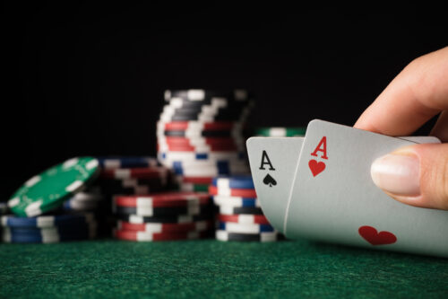 an image of a poker game casino chips and ace cards being held.
