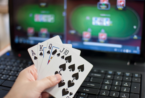 Playing cards behind held infront of a laptop showing a game of poker online.