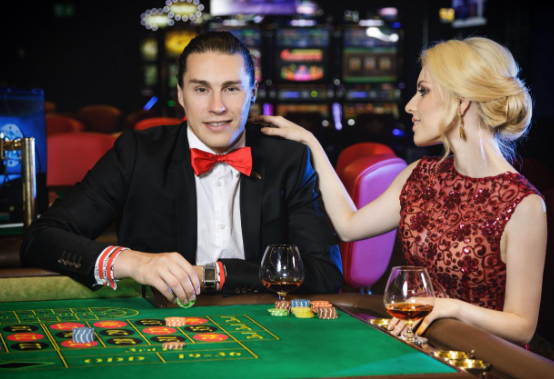 an image of a man in a suit and red bow tie playing a chip , a women next to him in a red dress has her hand on his shoulder, both showing casino etiquette