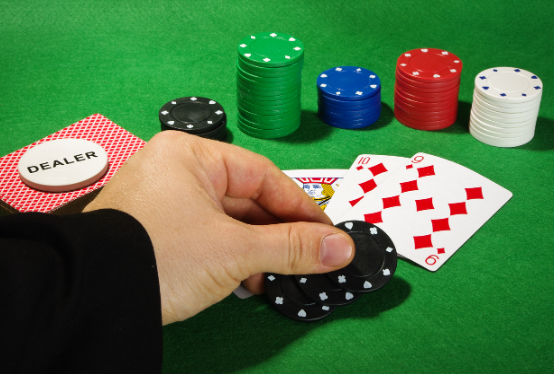 a close up of a hand holding black chips on a poker table with cards and green, blue, red chips
