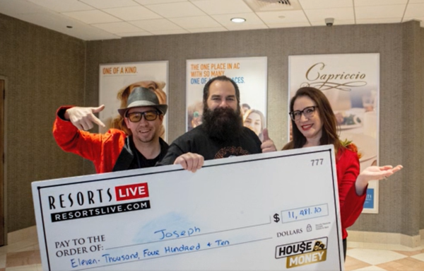 two men and women stand behind a big check for $11k, middle man has his thumbs up, house money winner